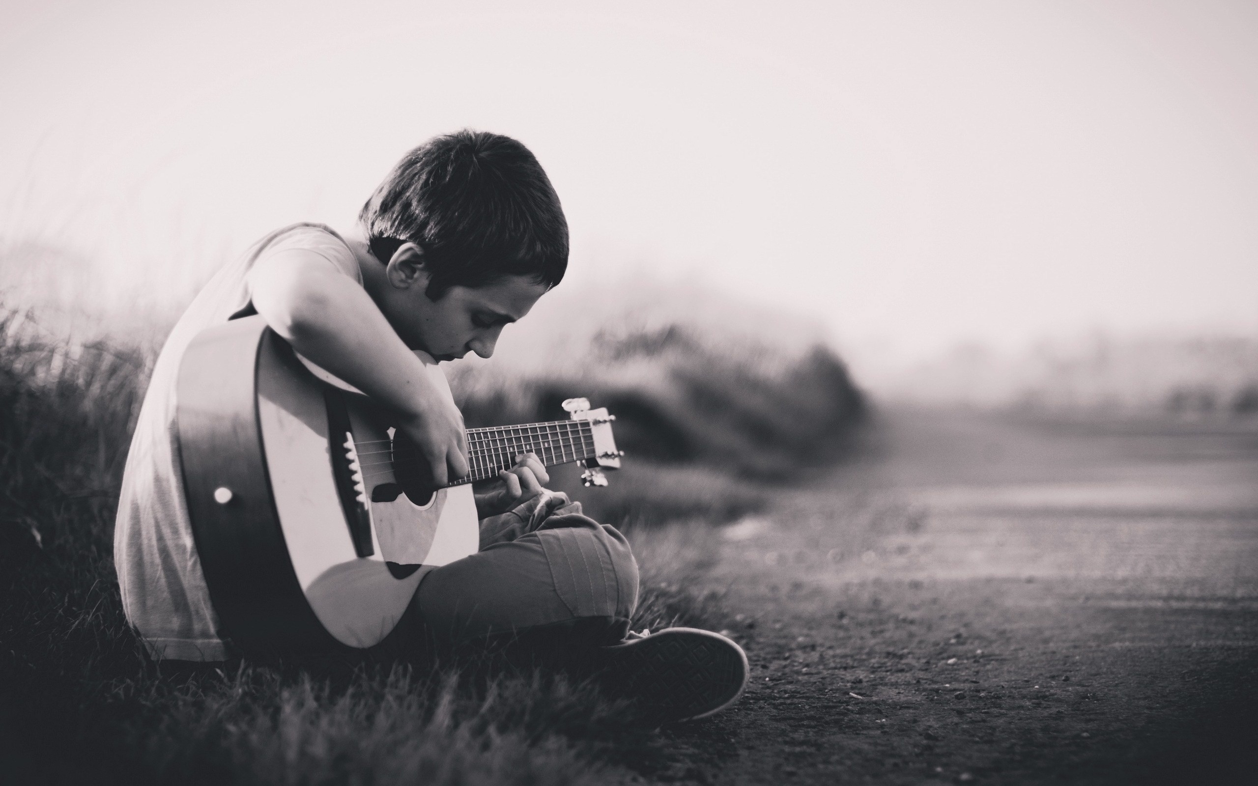 enfant qui joue de la guitare assis dans l'herbe
